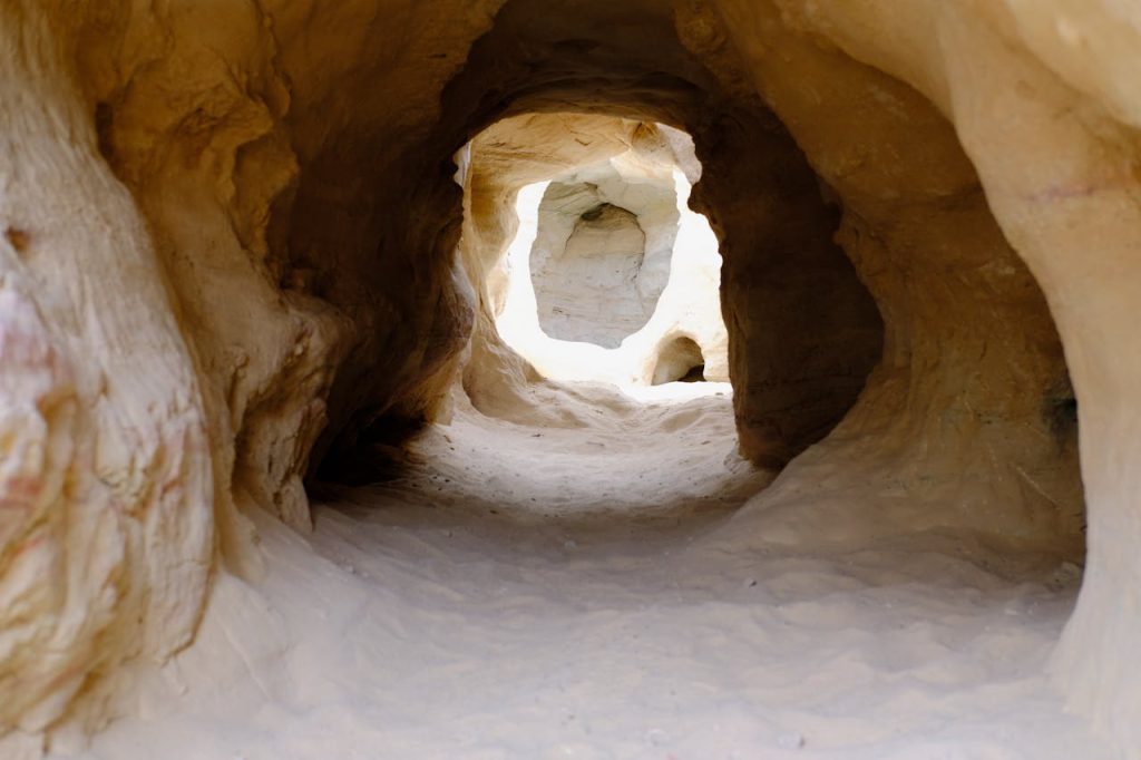 Explore a naturally eroded sandstone tunnel with sunlight filtering through, showcasing intricate geological formations.